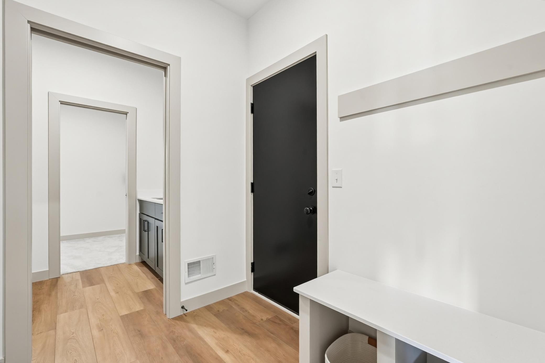 Mudroom & Drop Zone
Convenient mudroom transition area off the garage equipped with durable wood-plank flooring, a built-in seating bench with storage cubbies, and a sleek modern dark accent door.
