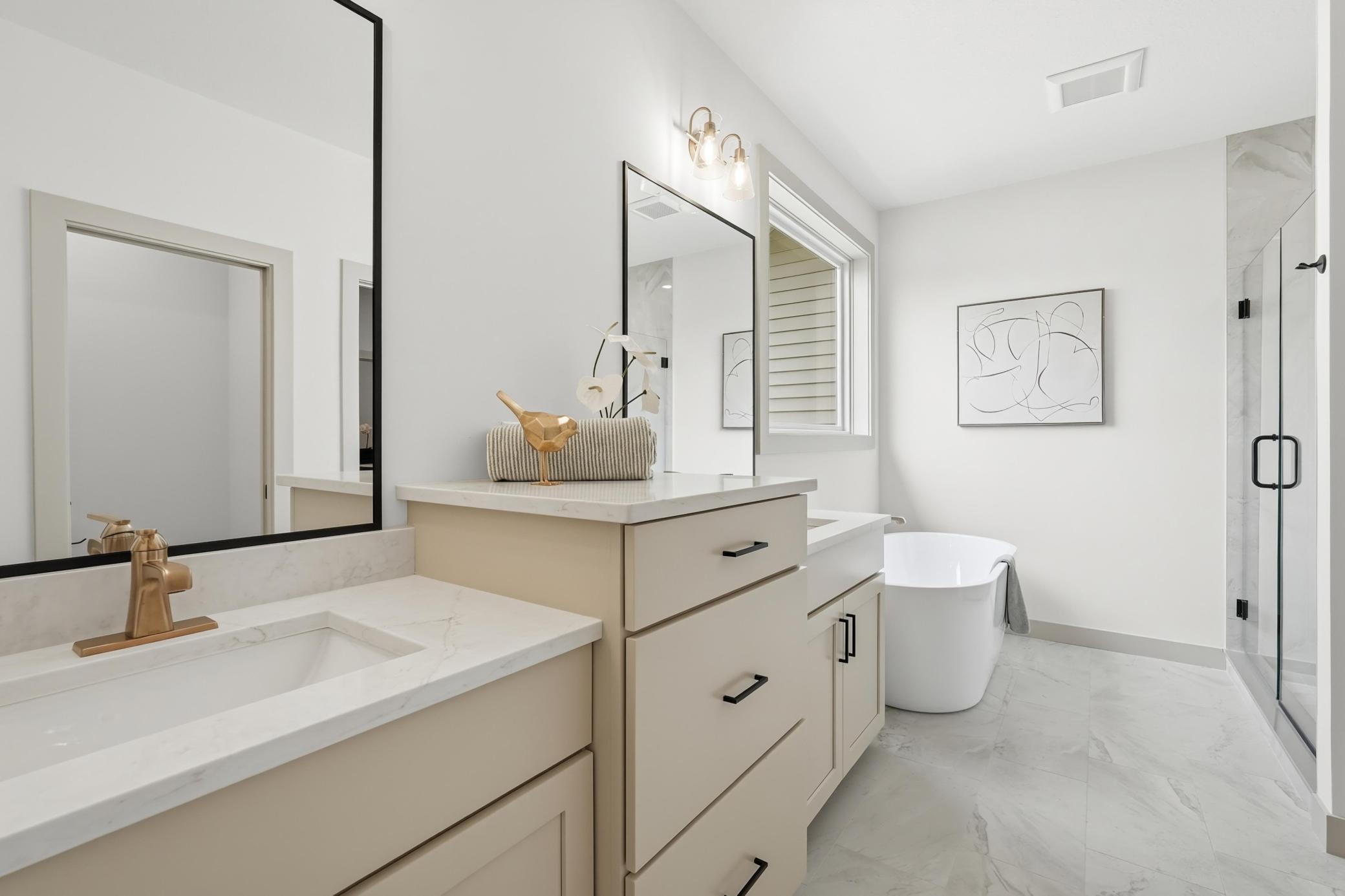 Primary En-Suite Spa Bath
Luxurious spa-inspired primary bathroom featuring staggered dual vanities, luxury champagne-bronze and black fixtures, a freestanding soaking tub under a sunlit window, and a custom glass-enclosed tiled shower.