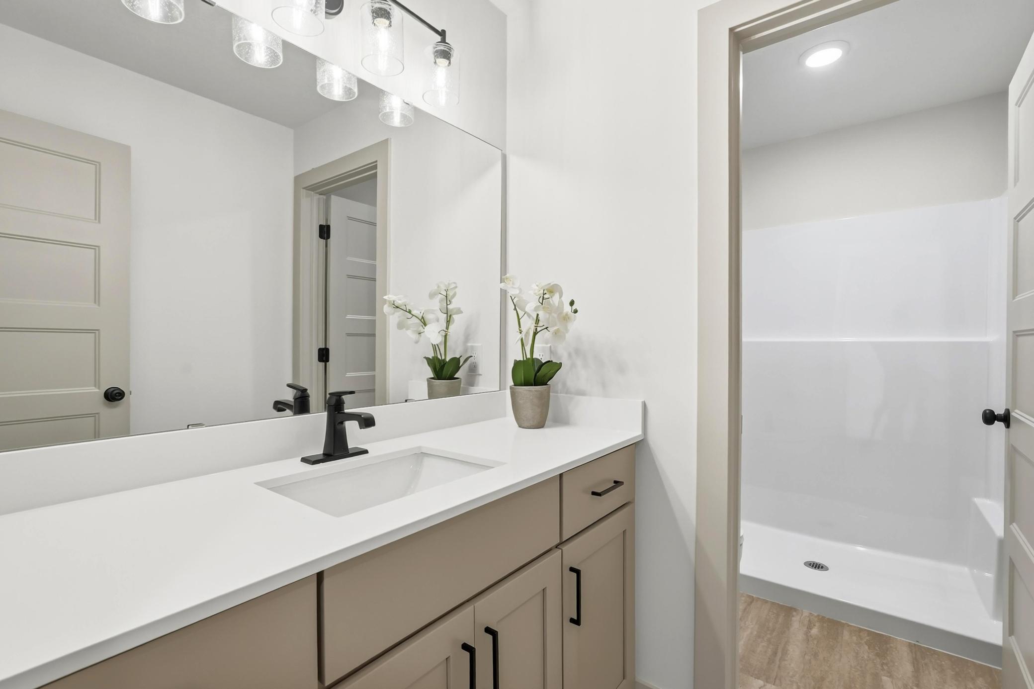 Well-appointed bathroom featuring a single-sink vanity with white quartz counters, matte black hardware, updated vanity lighting, and a separate walk-in shower room.