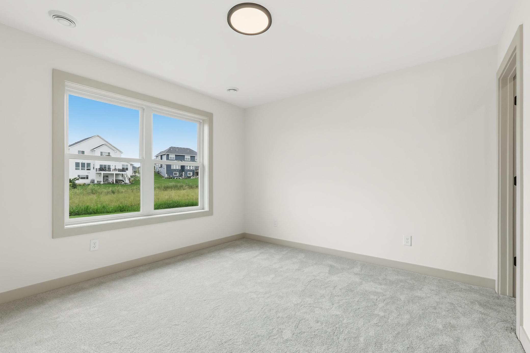 Sunlit Secondary Bedroom Bright and airy 3rd bedroom featuring soft neutral carpeting, clean crisp walls, modern lighting, and oversized windows overlooking peaceful green space.