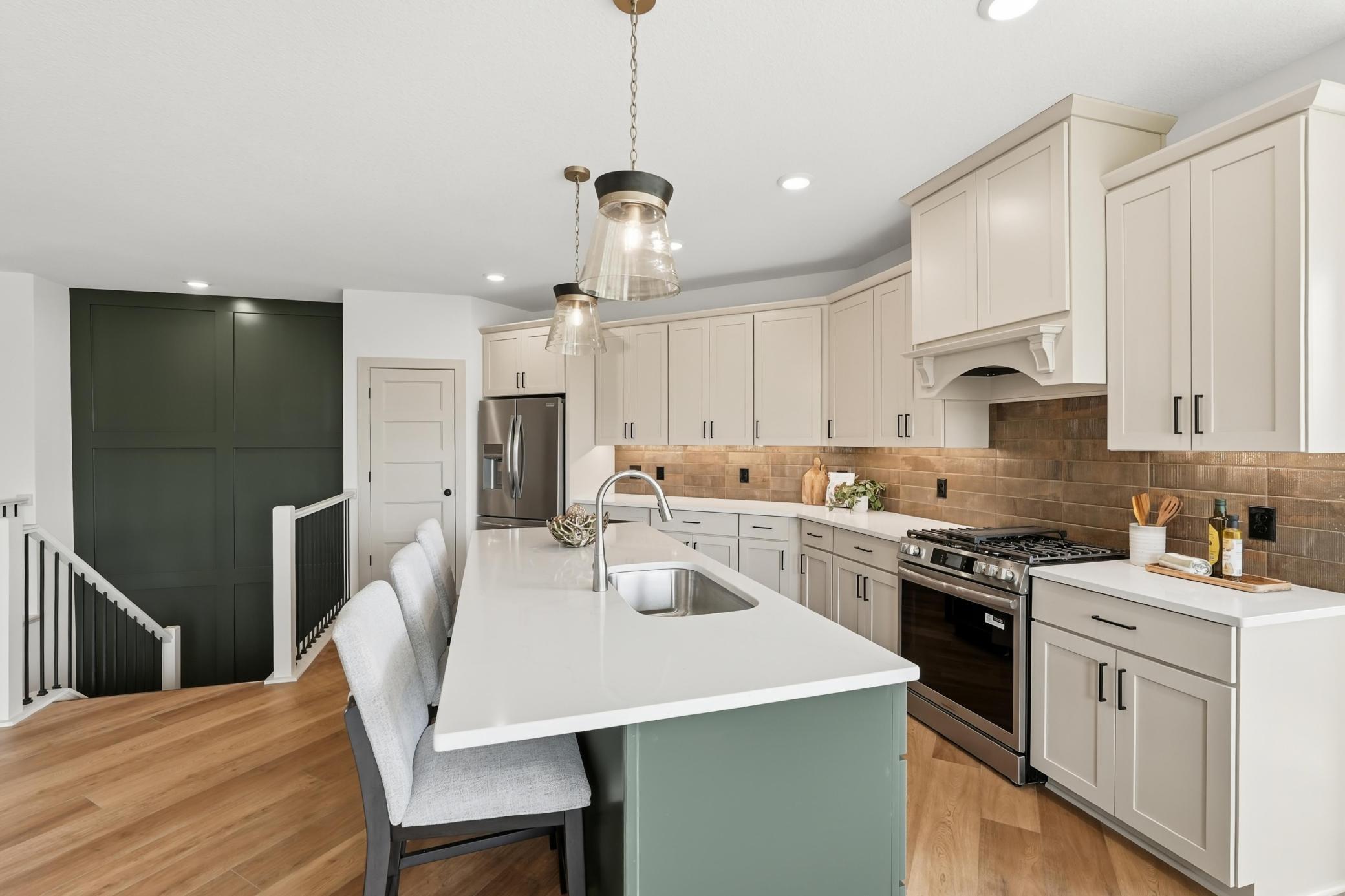 Practical luxury defines this kitchen, featuring an expansive central island with a sage-green base, quartz countertops, undermount sink, and seating, all seamlessly tied together by a dramatic dark feature wall and open sightlines.