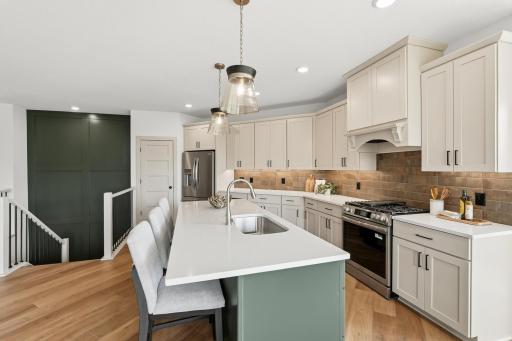 Practical luxury defines this kitchen, featuring an expansive central island with a sage-green base, quartz countertops, undermount sink, and seating, all seamlessly tied together by a dramatic dark feature wall and open sightlines.