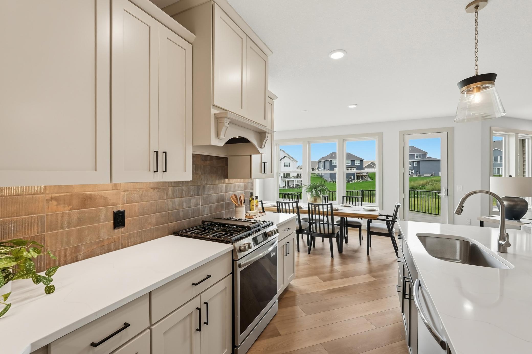 High-end chef's kitchen outfitted with soft-close shaker cabinetry, gas cooktop with custom decorative hood, textured subway tile backsplash with under-cabinet lighting, and a central quartz-topped island with undermount sink.