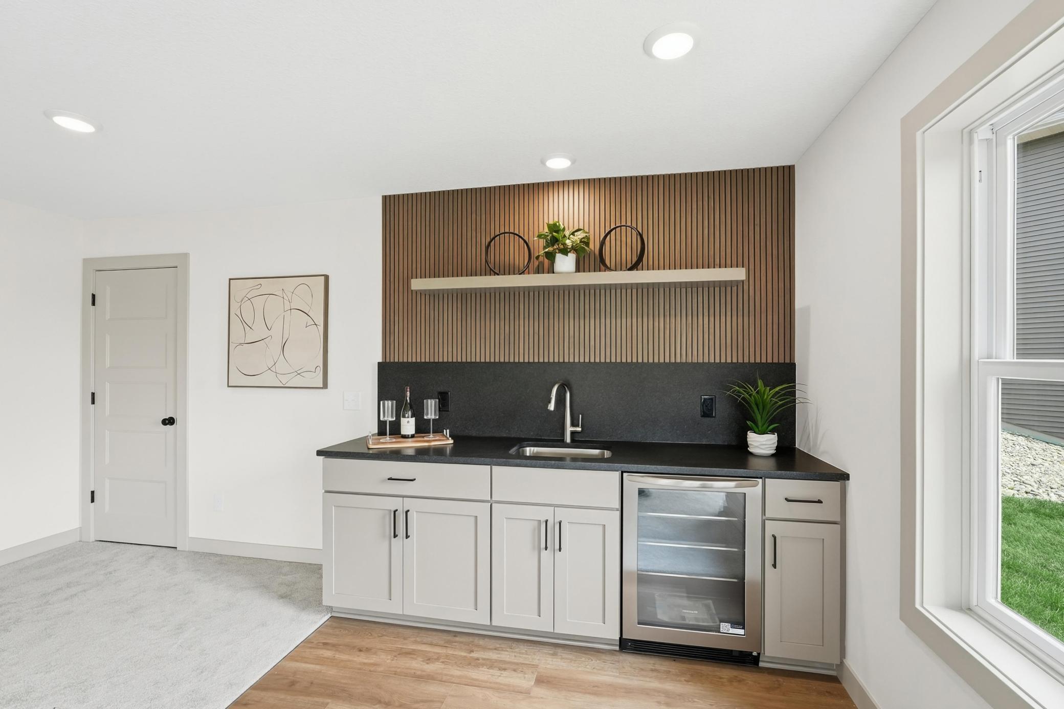 Entertaining Wet Bar Custom lower-level wet bar crafted with a slatted-wood accent wall, floating display shelf, dark quartz countertops, undermount bar sink, built-in beverage fridge, and shaker soft close cabinetry.