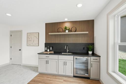 Entertaining Wet Bar Custom lower-level wet bar crafted with a slatted-wood accent wall, floating display shelf, dark quartz countertops, undermount bar sink, built-in beverage fridge, and shaker soft close cabinetry.