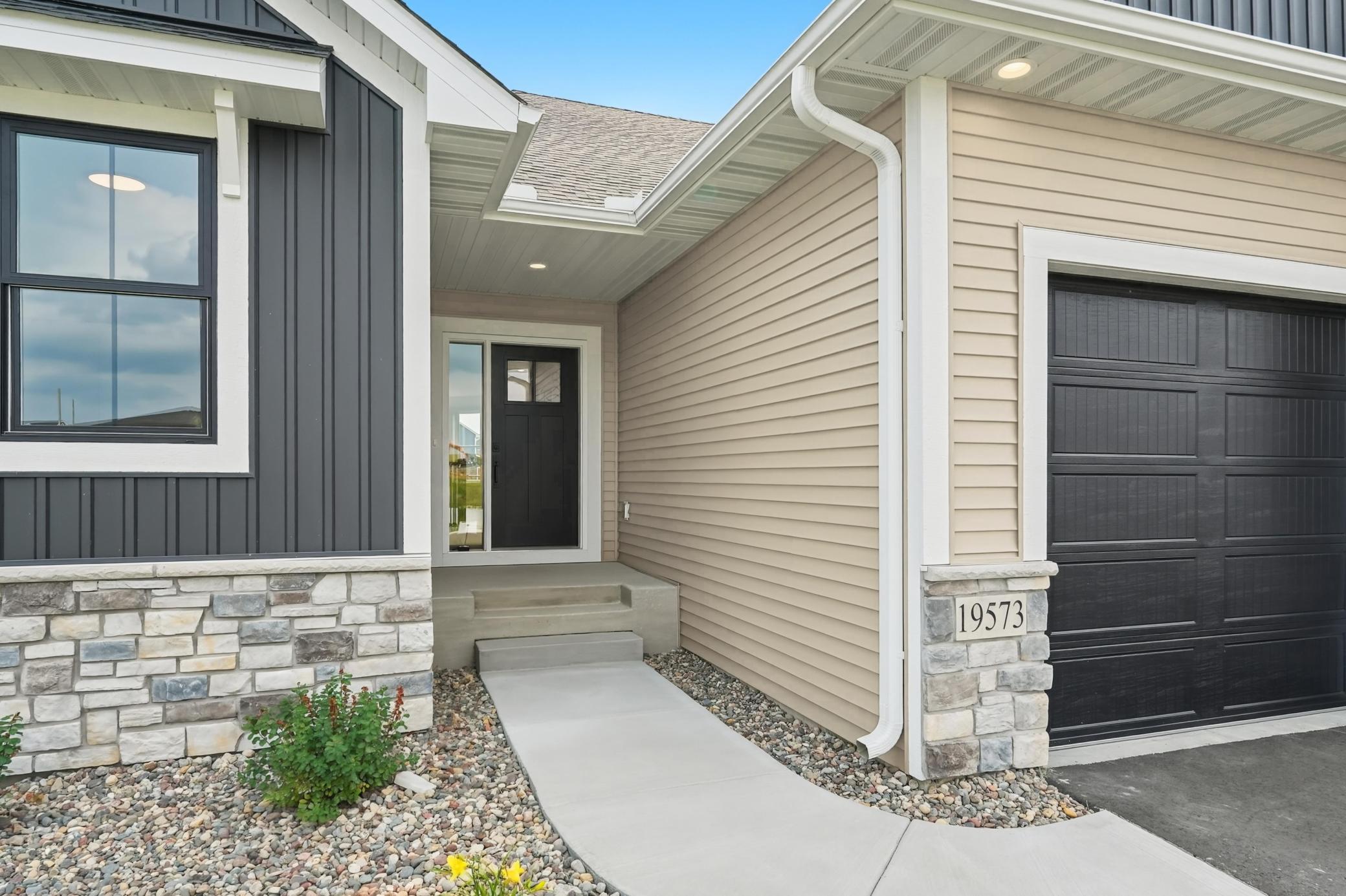 Covered Front Entry
Inviting covered front entry featuring a modern dark front door with a glass sidelight, recessed soffit lighting, stack-stone accents, and a clean concrete walkway.