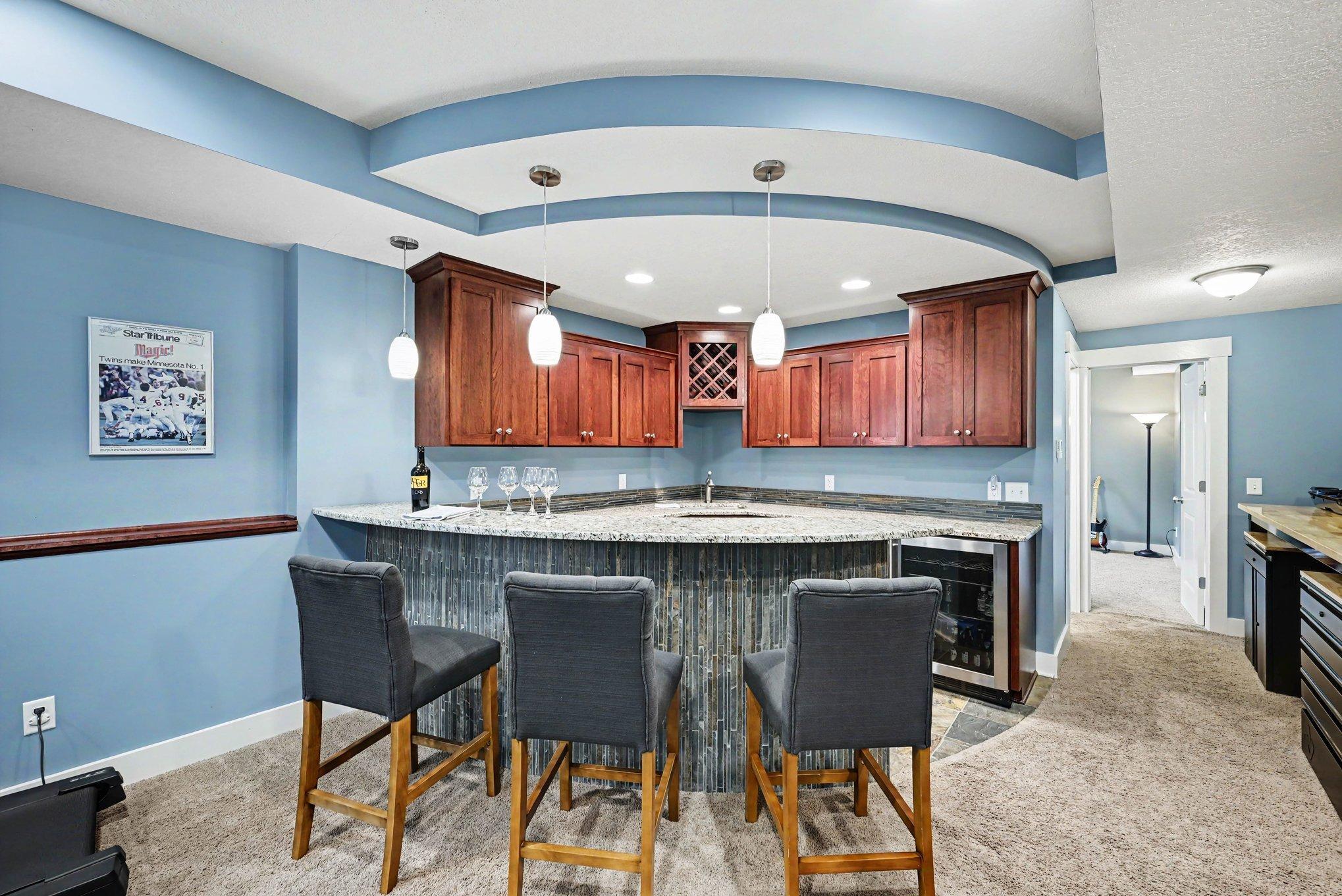 Wet bar with granite counters, cherry cabinets, and beverage fridge