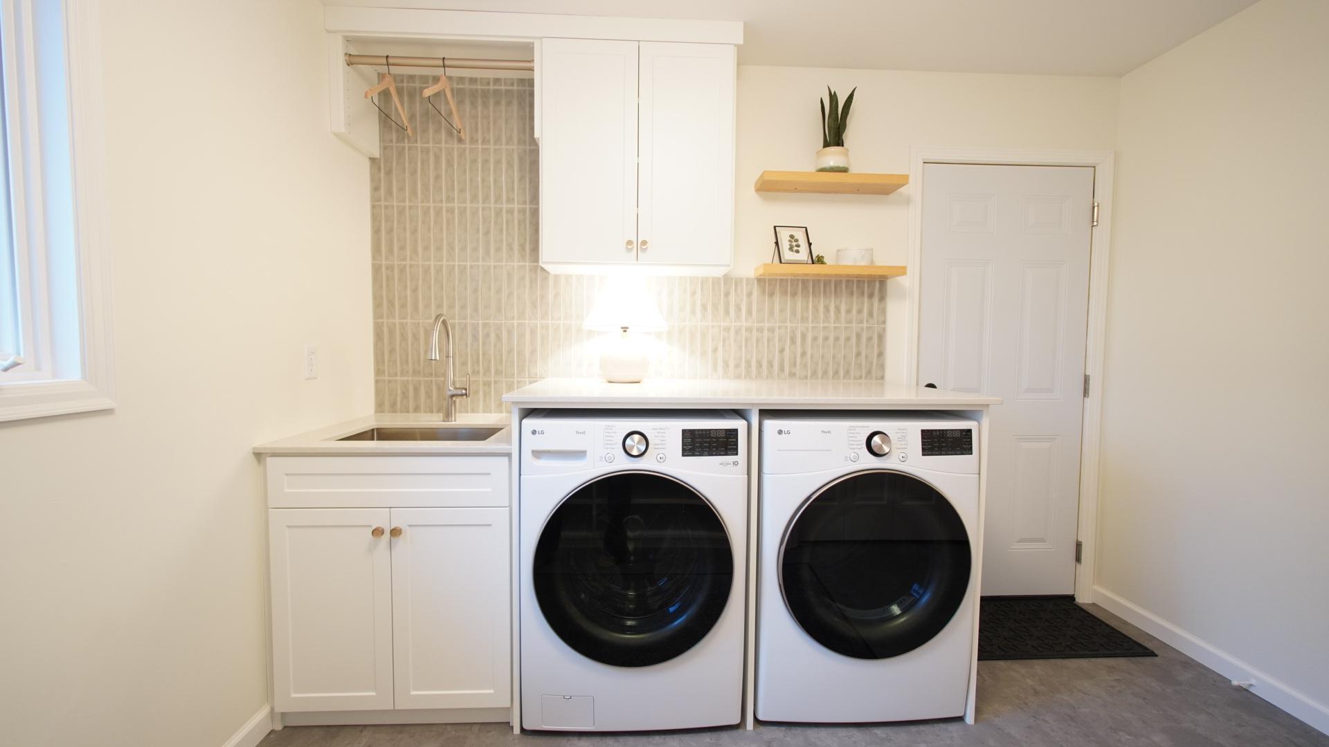 The mud room at the garage entry provides an integrated laundry system with ample storage, a ceramic tile backsplash, floating shelves and a quartz countertop. This is one of two washer/dryer sets in the home.