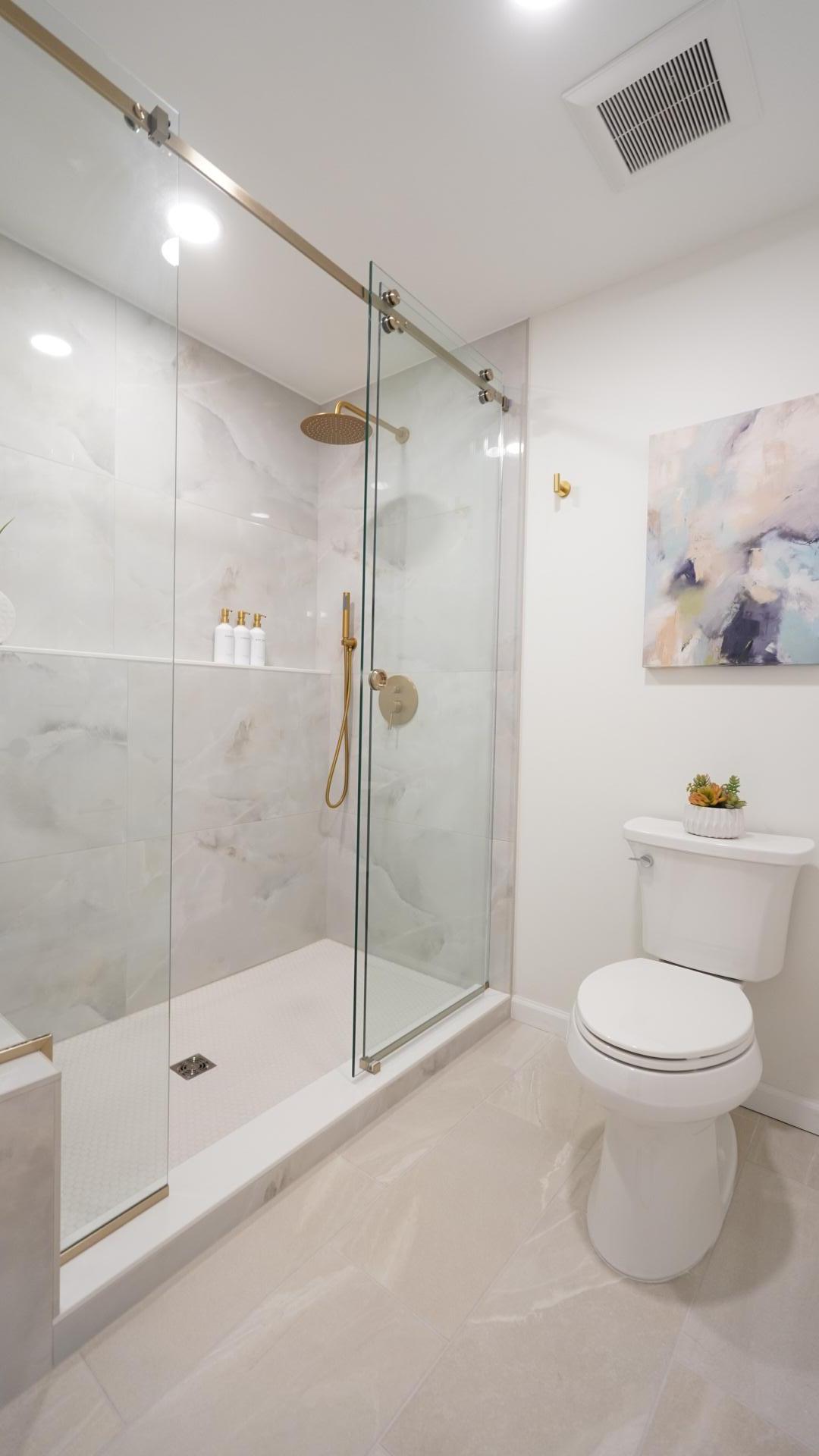 The primary bath shower and toilet room features a massive shower with large format tile, brushed gold shower trim and a custom glass shower door.