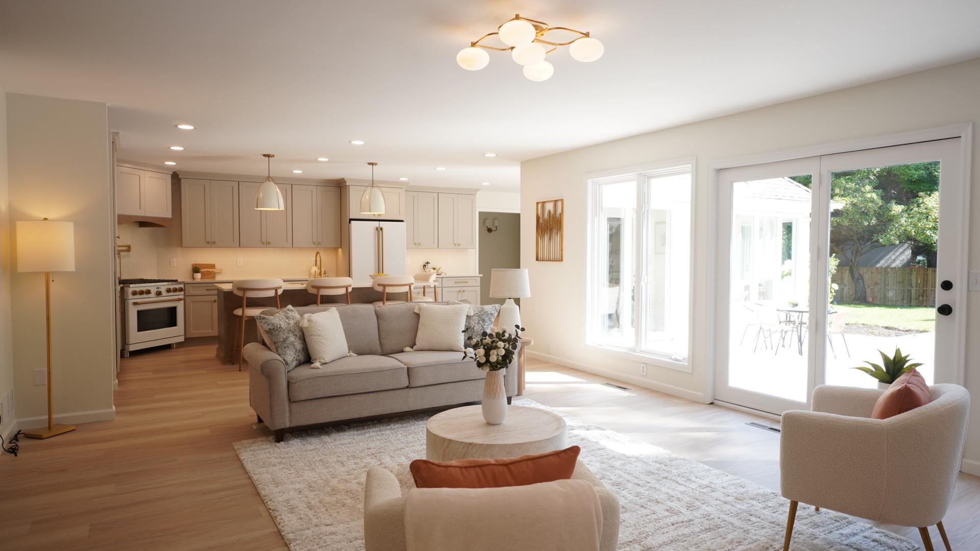 The custom kitchen opens to the spacious living room, which is bright and welcoming thanks to fresh paint, brand new flooring in a light tone, and a ton of natural light streaming in from the back patio.