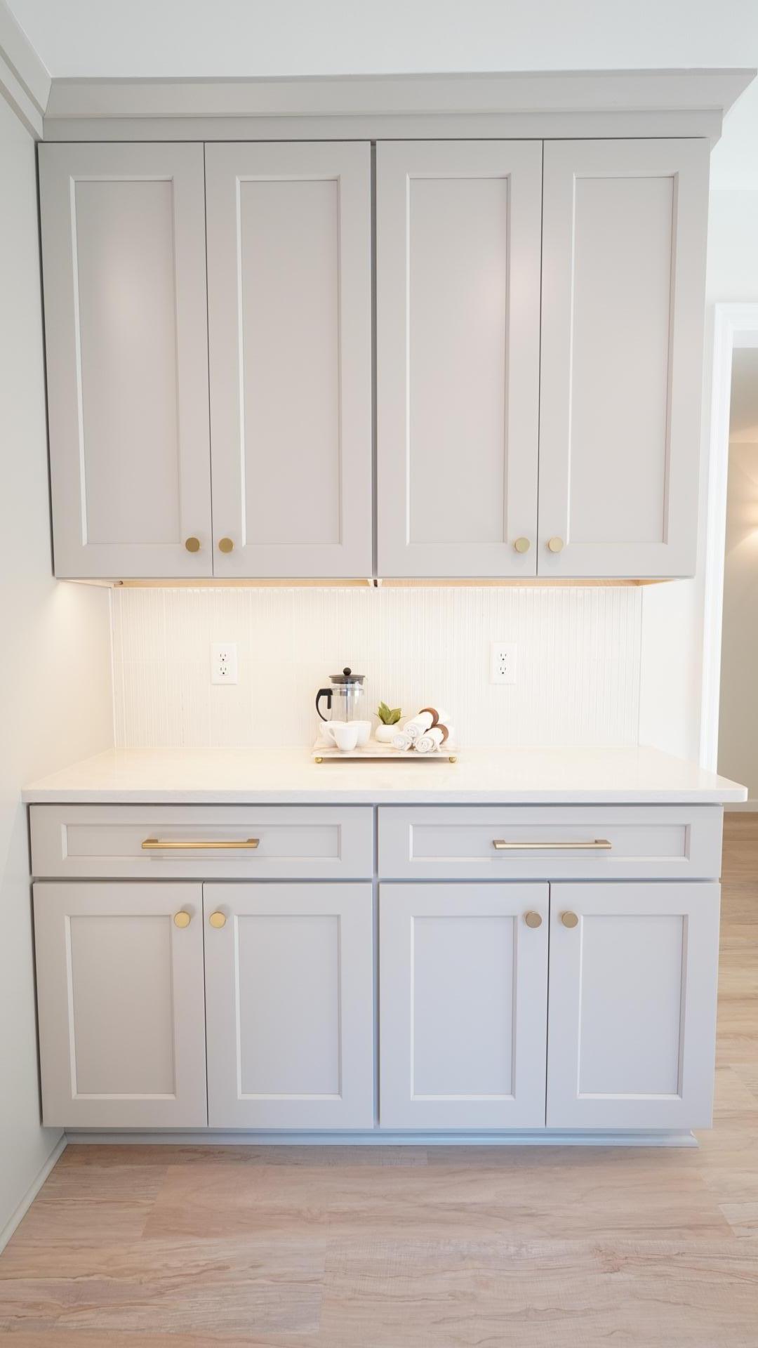The light gray, factory-painted wood cabinetry and brushed gold hardware, staged here as a coffee bar, is fully custom with both ample storage and soft close doors.