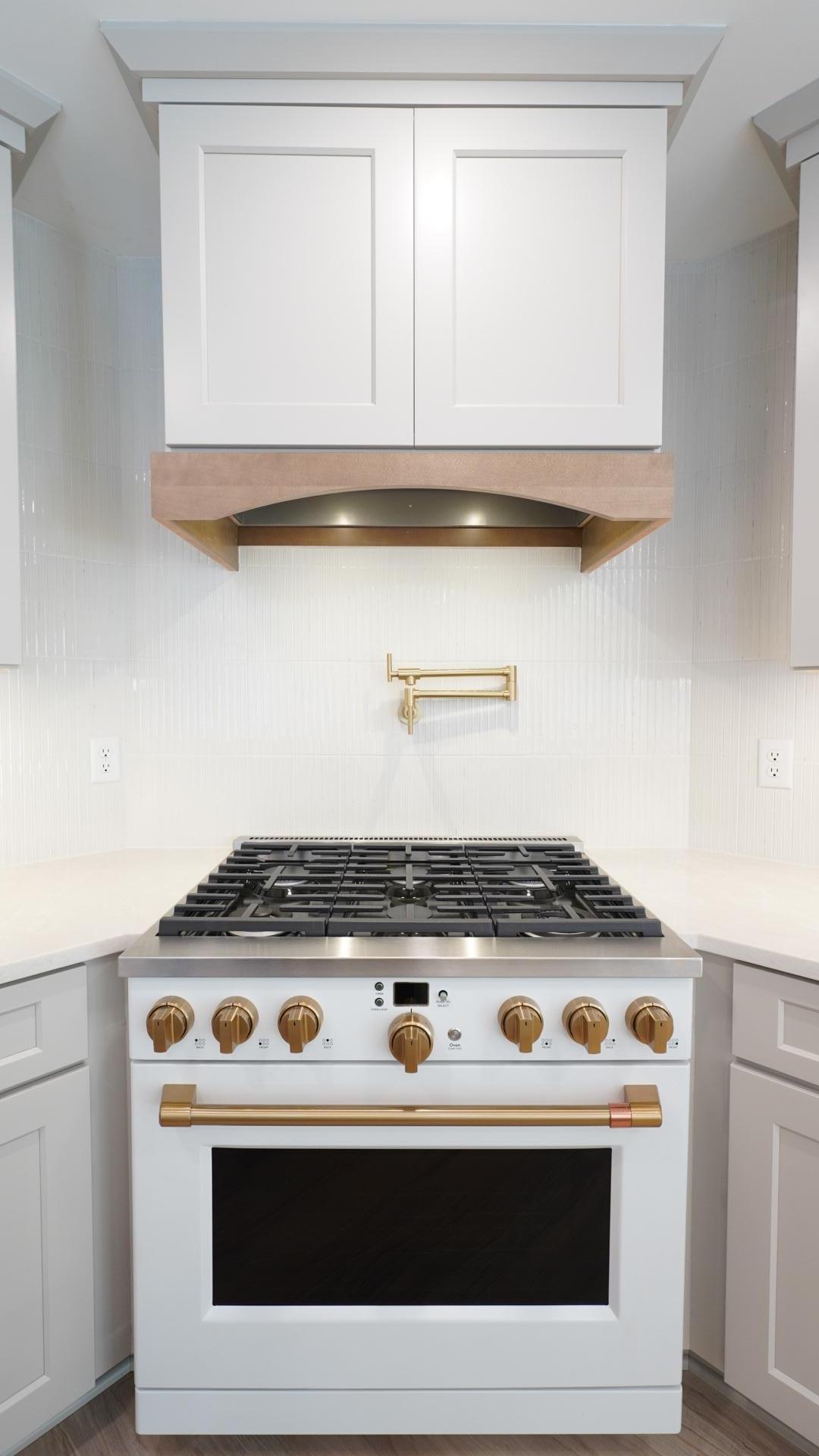 The open kitchen includes a CAFE', extra-wide commercial style gas range with a custom hood surround and a coordinating pot filler.