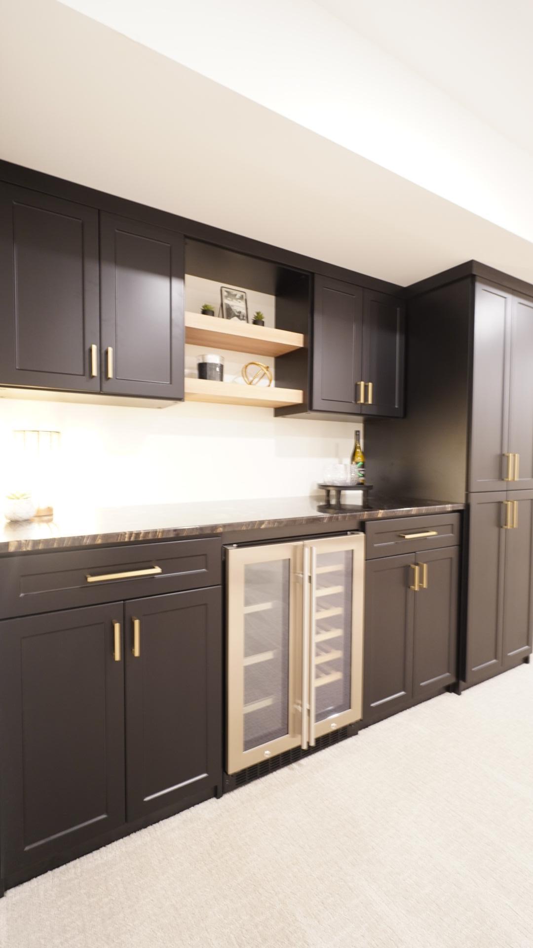 The custom dry bar is a modern and sophisticated focal point in the basement family room featuring beautiful dark granite countertops, ample storage and a built-in beverage refrigerator.