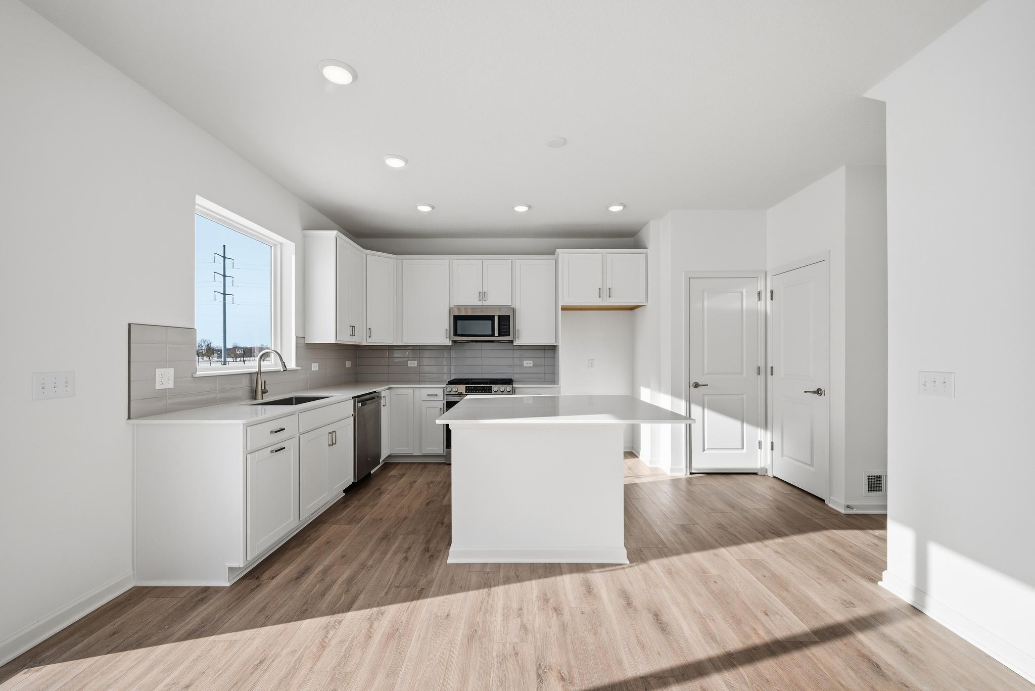 The kitchen combines style and functionality with white cabinetry, quartz countertops, and a spacious center island that offers additional prep space and seating. Images of similar home, interior selections differ.