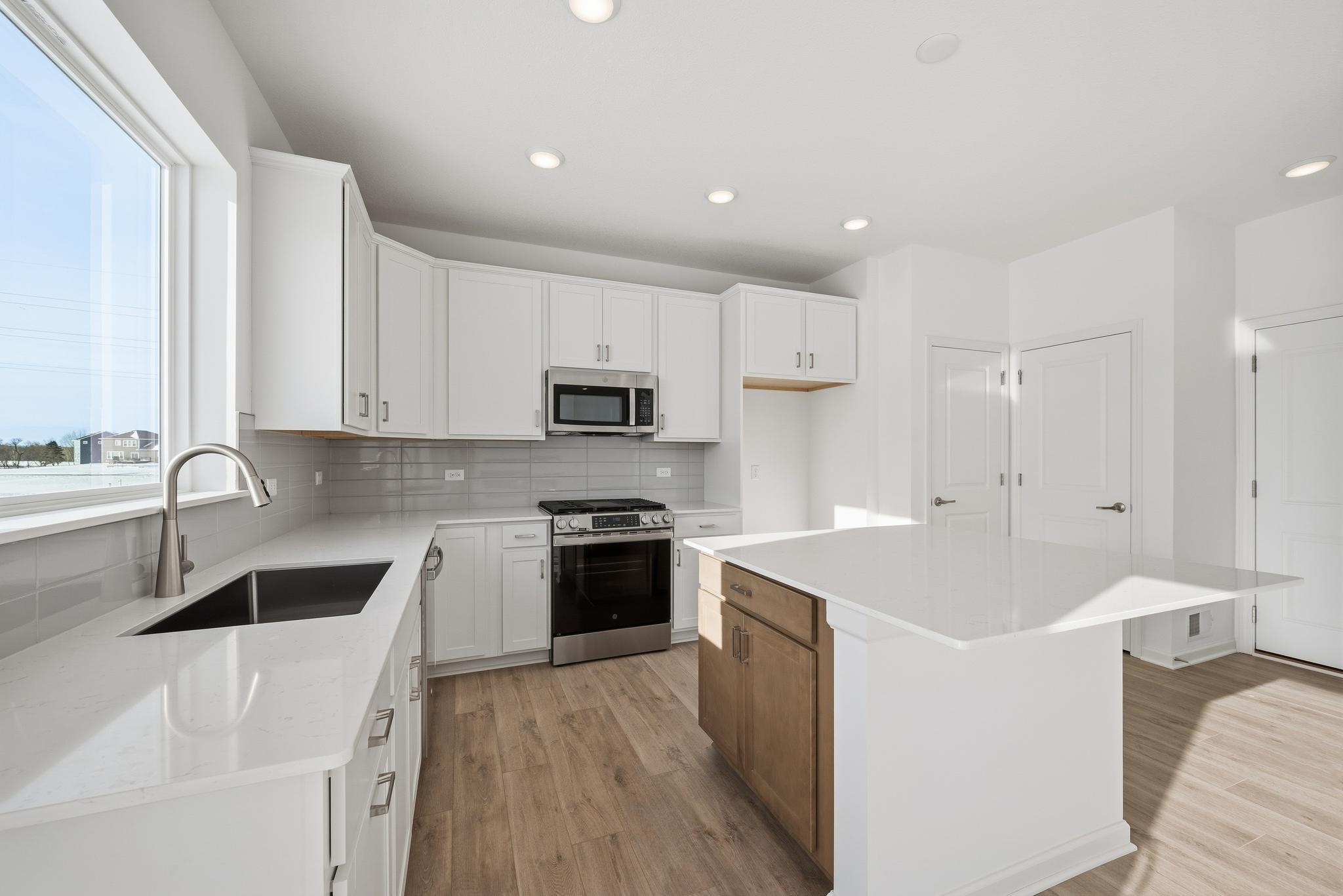 The kitchen combines style and functionality with white cabinetry, quartz countertops, and a spacious center island that offers additional prep space and seating. Images of similar home, interior selections differ.
