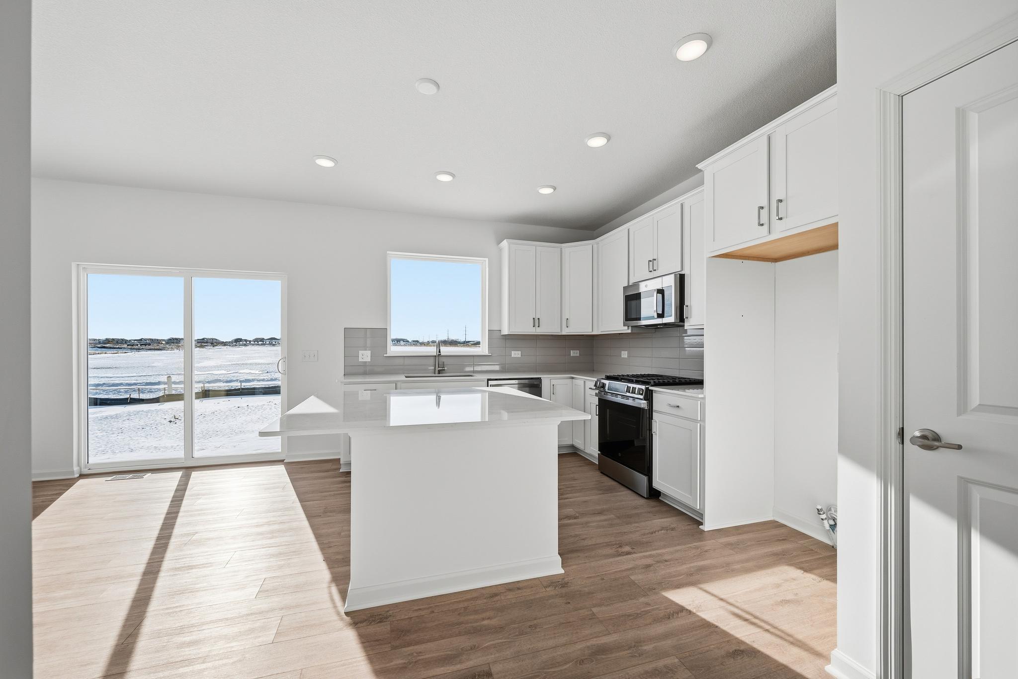 The kitchen combines style and functionality with white cabinetry, quartz countertops, and a spacious center island that offers additional prep space and seating. Images of similar home, interior selections differ.