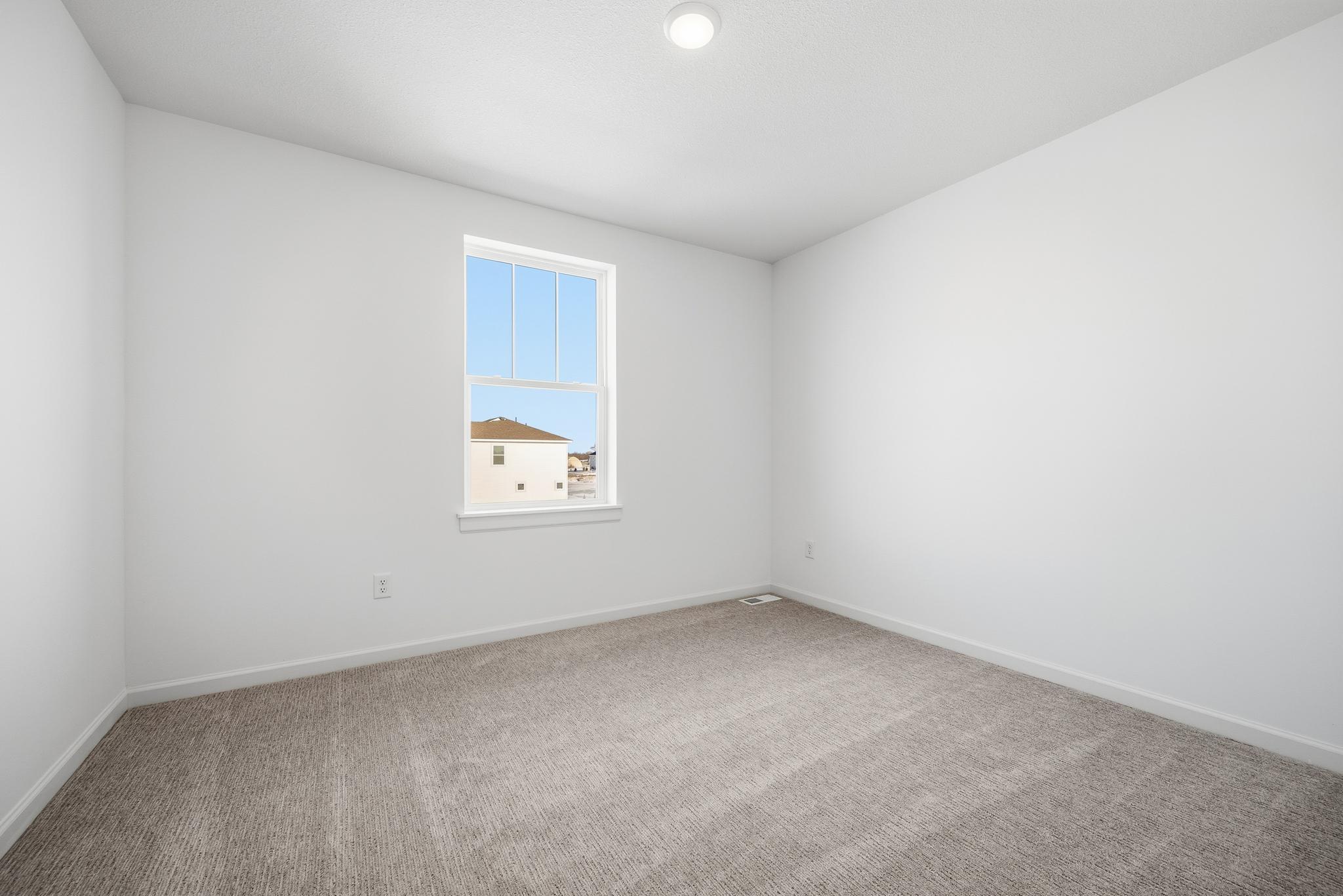 This secondary bedroom features a comfortable layout with well-placed windows, allowing natural light to brighten the space.Images of similar home, interior selections differ.