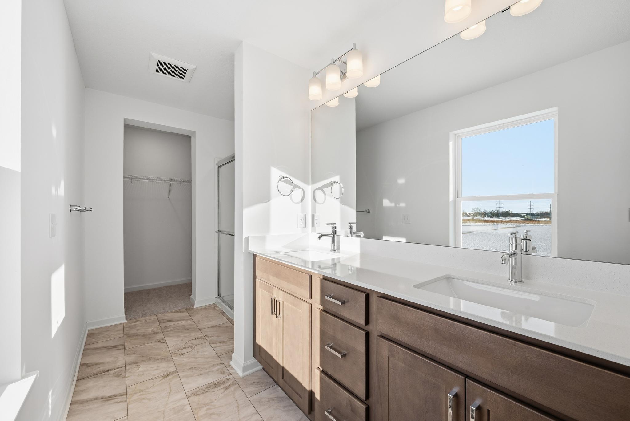 The primary bathroom features a dual-sink vanity with quartz countertops, ample cabinetry, and modern fixtures. Images of similar home, interior selections differ.