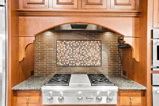 Statement cooking area with gas range, tile backsplash and custom wood surround
