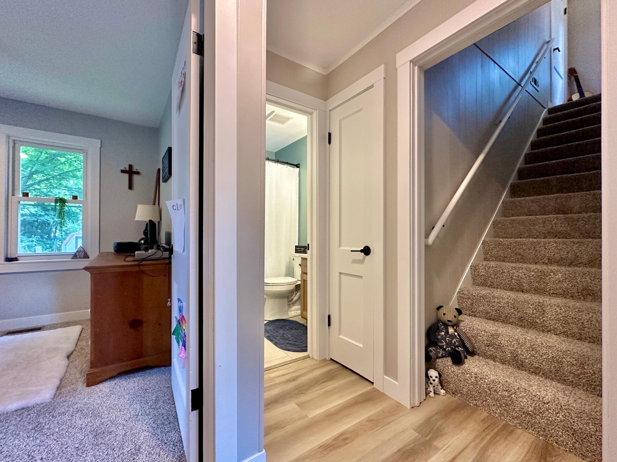This hall view gives a glimpse into the other bedroom on the main and the main level bath with the stairs to the upper level on the right.