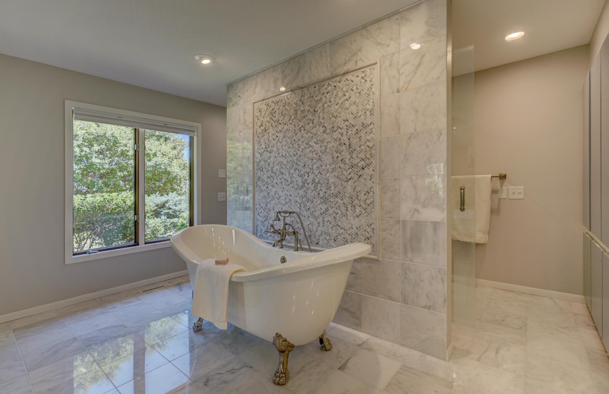 This remodeled spa-inspired bathroom featuring double vanities, an elegant clawfoot soaking tub, exquisite marble tile, and a stunning floor-to-ceiling tiled walk-in shower