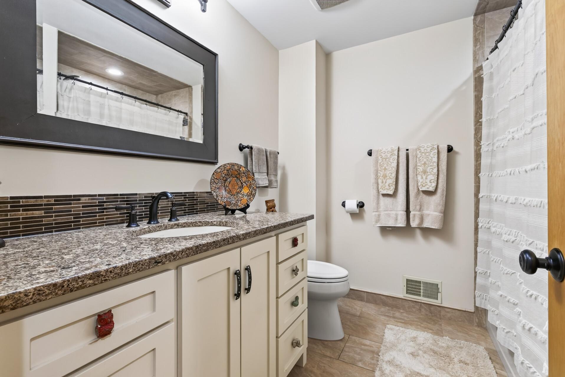 Updated full bath featuring custom cabinetry, granite countertops, tilework, and contemporary fixtures.