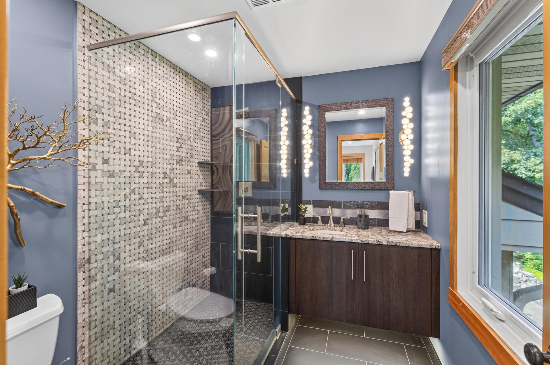 Beautifully updated primary ensuite featuring stunning tilework, granite finishes, and a glass-enclosed shower.