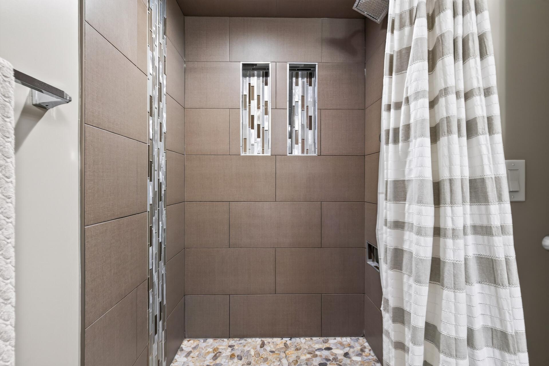 The walk-in shower stands out with textured tile, decorative glass accents, a pebble floor, and rainfall showerhead.