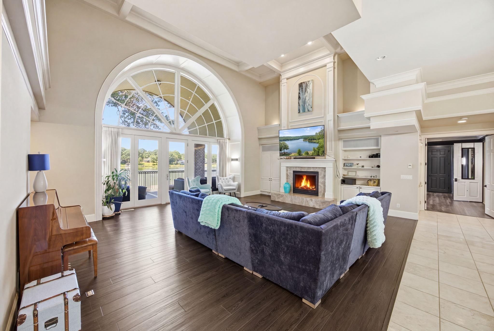 The dramatic great room pairs a soaring arched wall of windows with a fireplace and peaceful lake views