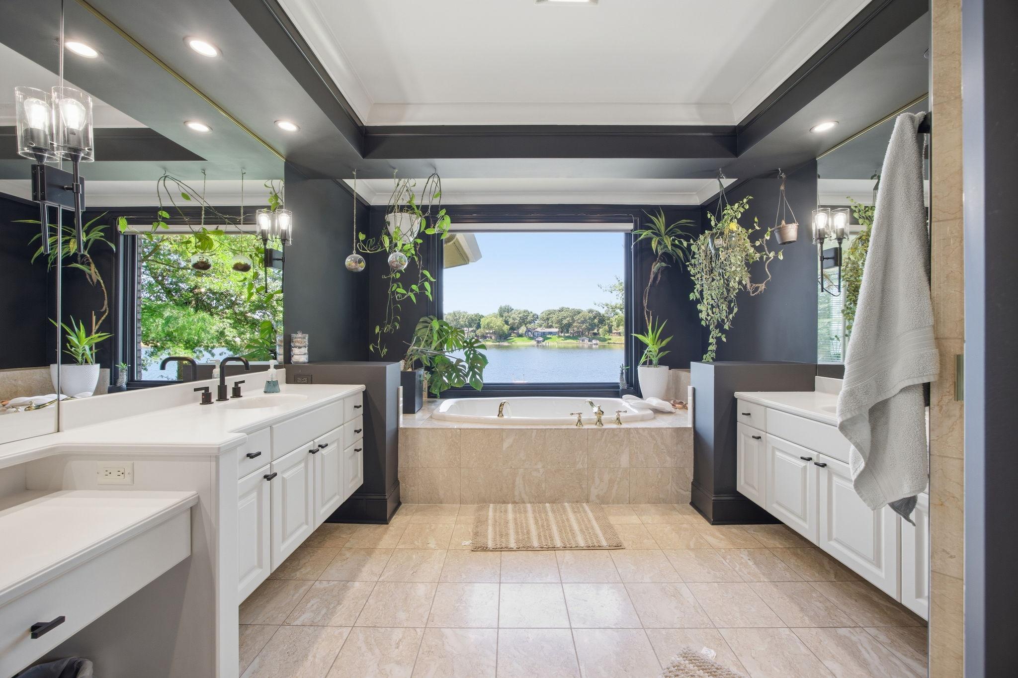 Designed for relaxation, the primary ensuite bath showcases beautiful tile floors, a jetted soaking tub beneath a picture window, dual vanities, and a walk-in shower