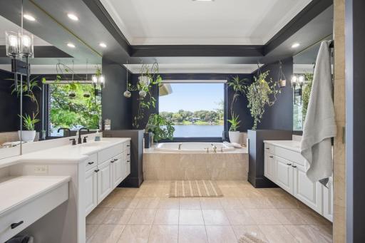 Designed for relaxation, the primary ensuite bath showcases beautiful tile floors, a jetted soaking tub beneath a picture window, dual vanities, and a walk-in shower