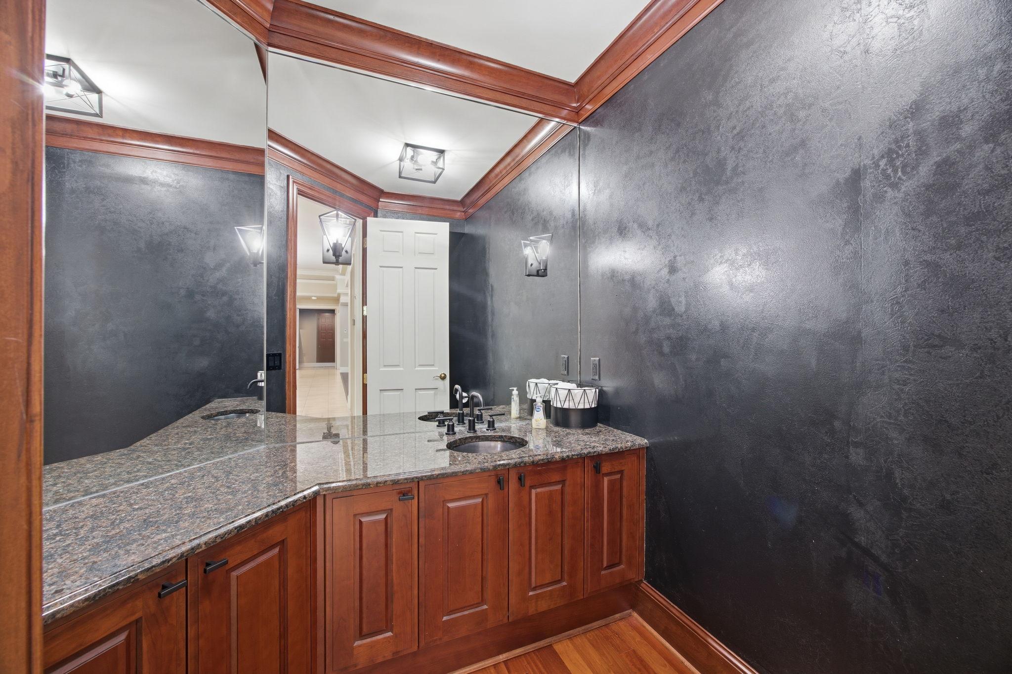 A richly finished powder room brings a touch of drama with dark walls, warm wood cabinetry, and stone counters.