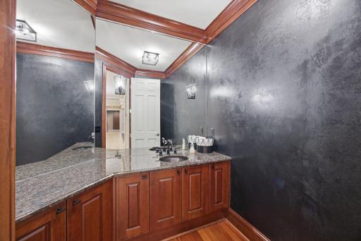A richly finished powder room brings a touch of drama with dark walls, warm wood cabinetry, and stone counters.