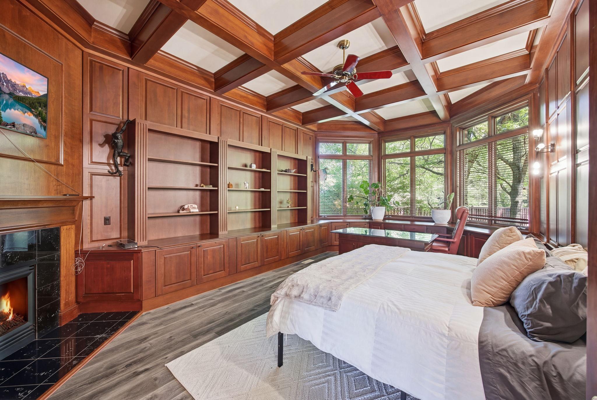 Main-level bedroom two is exquisitely designed with rich wood details, beautiful windows, and a cozy fireplace, creating a warm and inviting space