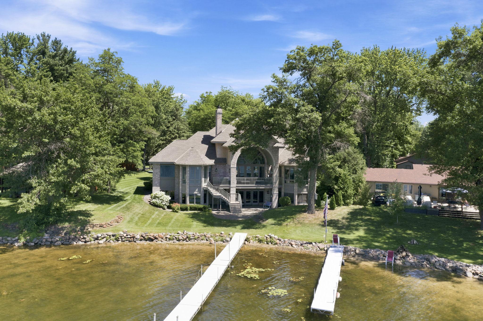 View from the back showcases the home's grand arched windows, multiple outdoor levels, and expansive lakeside lawn