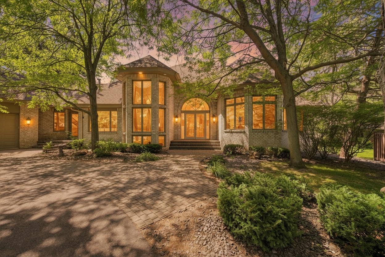A glowing twilight exterior highlights the home's striking architecture, grand entry, and mature tree-lined setting