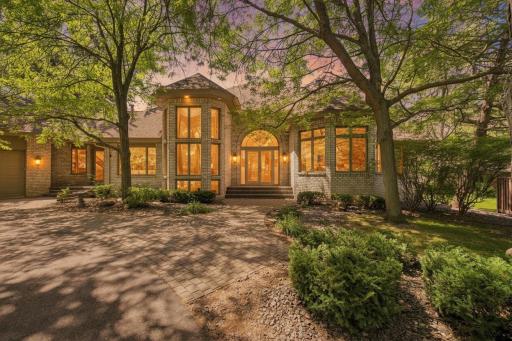A glowing twilight exterior highlights the home's striking architecture, grand entry, and mature tree-lined setting