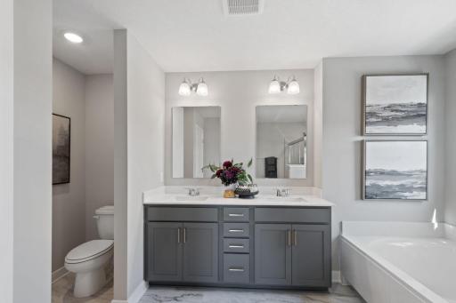 The primary en-suite bathroom offers a relaxing soaking tub, a fully tiled walk-in shower, quartz counters, dual sinks, and a linen closet for all your bathroom essentials. Photo of model home, colors and finishes may vary.