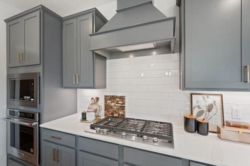 Beautifully tiled backsplash, elegant wood vent hood, and a 5-burner gas cooktop in this kitchen.