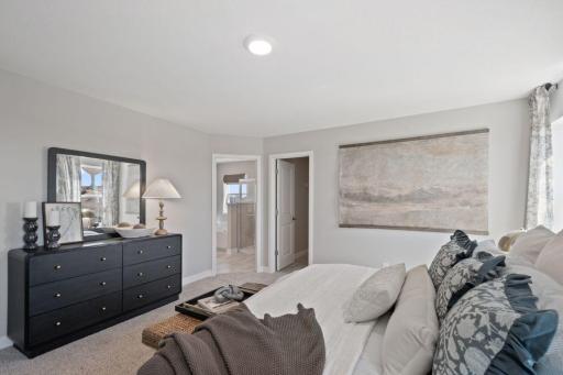 The primary bedroom suite features a spacious walk-in closet and a private bathroom. Photo of model home, color and finishes will vary.