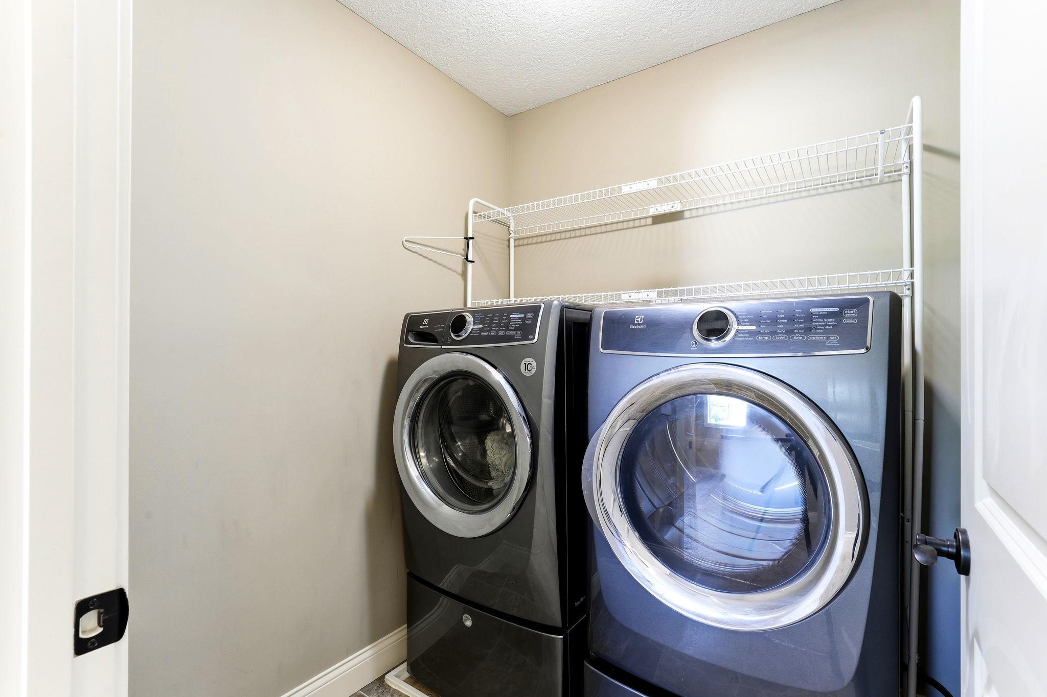 Dedicated upper level laundry room complete with included front-load Electrolux washer, dryer, and overhead wire shelving.