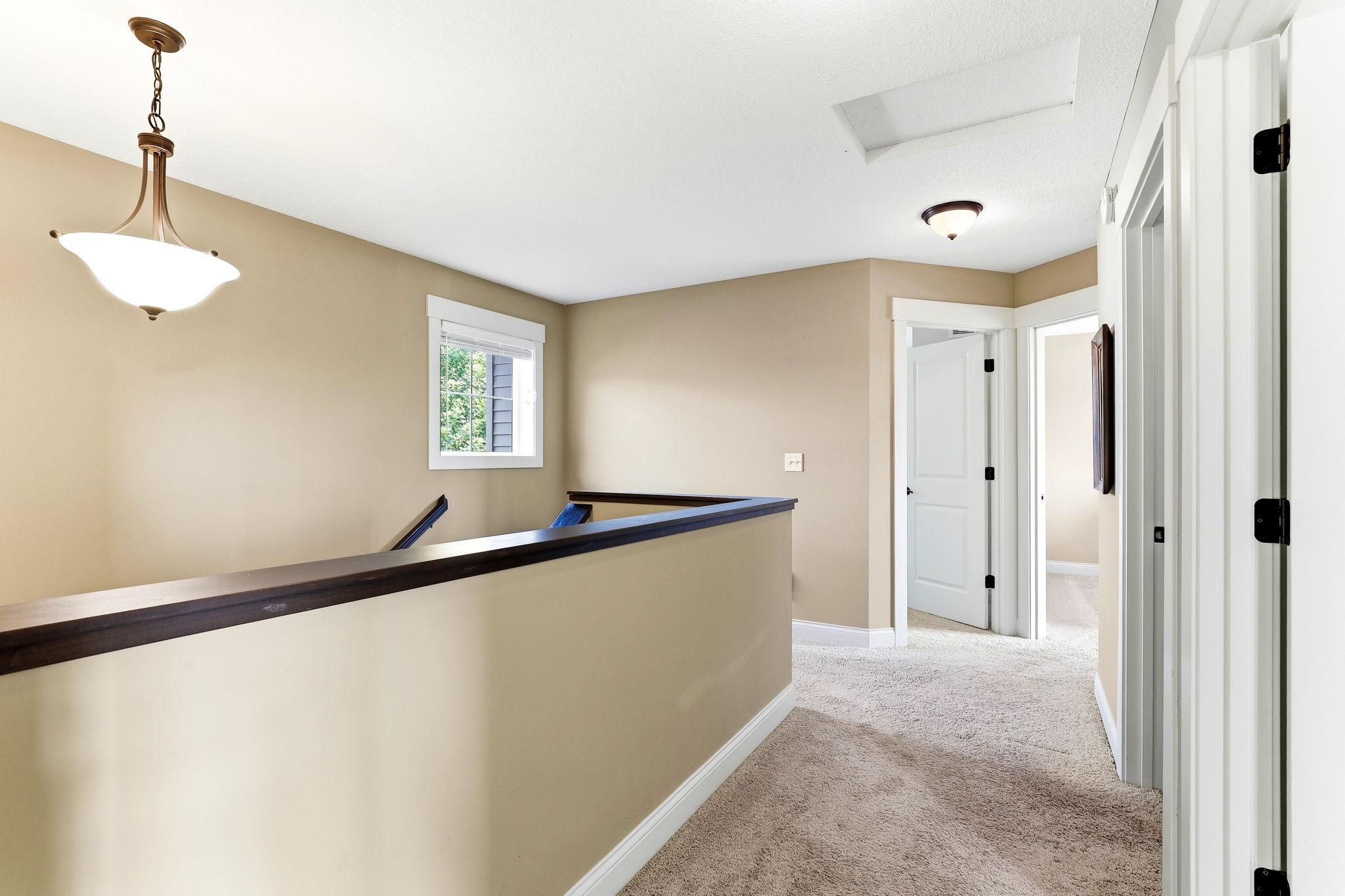 Spacious upper-level hallway featuring plush carpeting, bright window light, and seamless room access.
