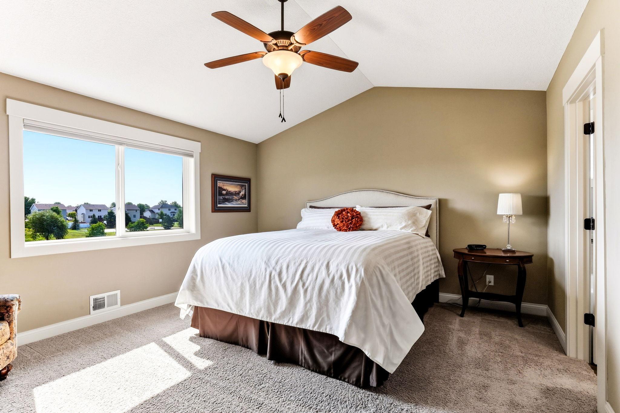 Primary bedroom suite featuring vaulted ceiling, ceiling fan, plush carpeting, and abundant natural light.