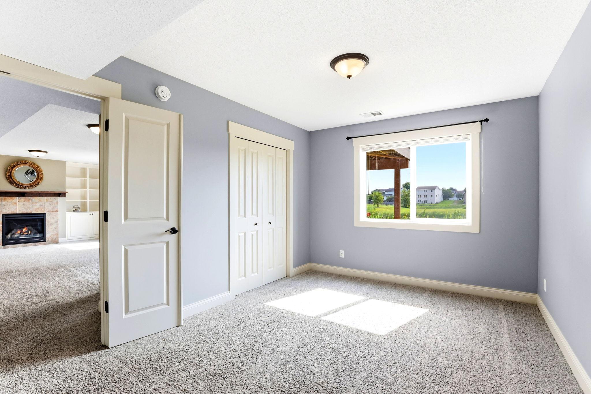 Lower-level fourth bedroom features plush carpeting, double bi-fold closet doors, comfortable neutral finishes, and a scenic backyard view.