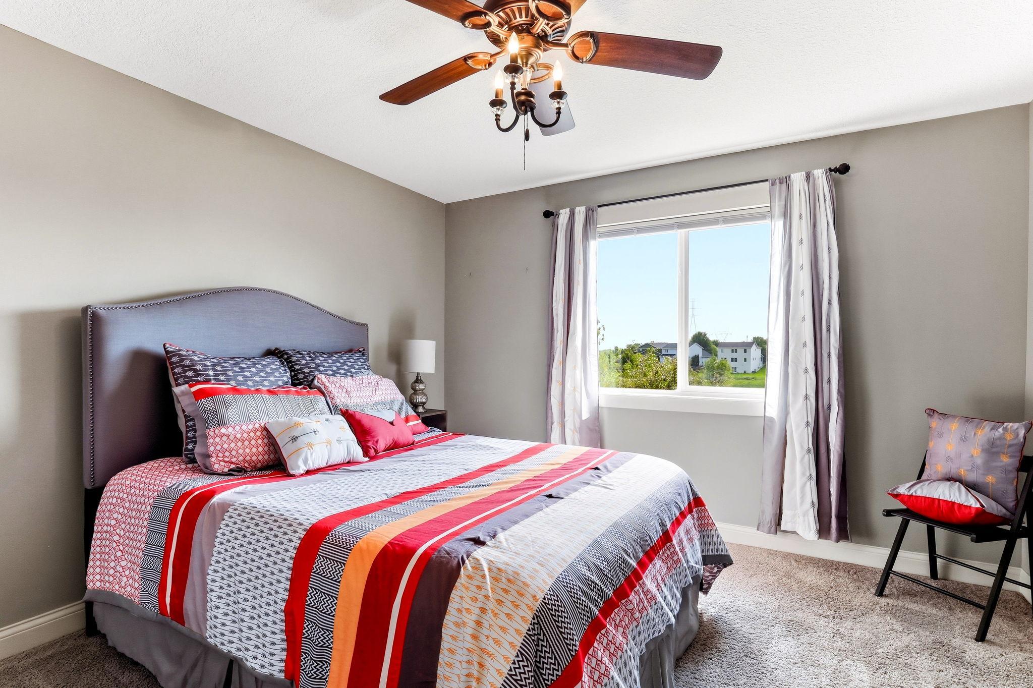 Bright second bedroom featuring ceiling fan, plush carpeting, and serene outdoor views.