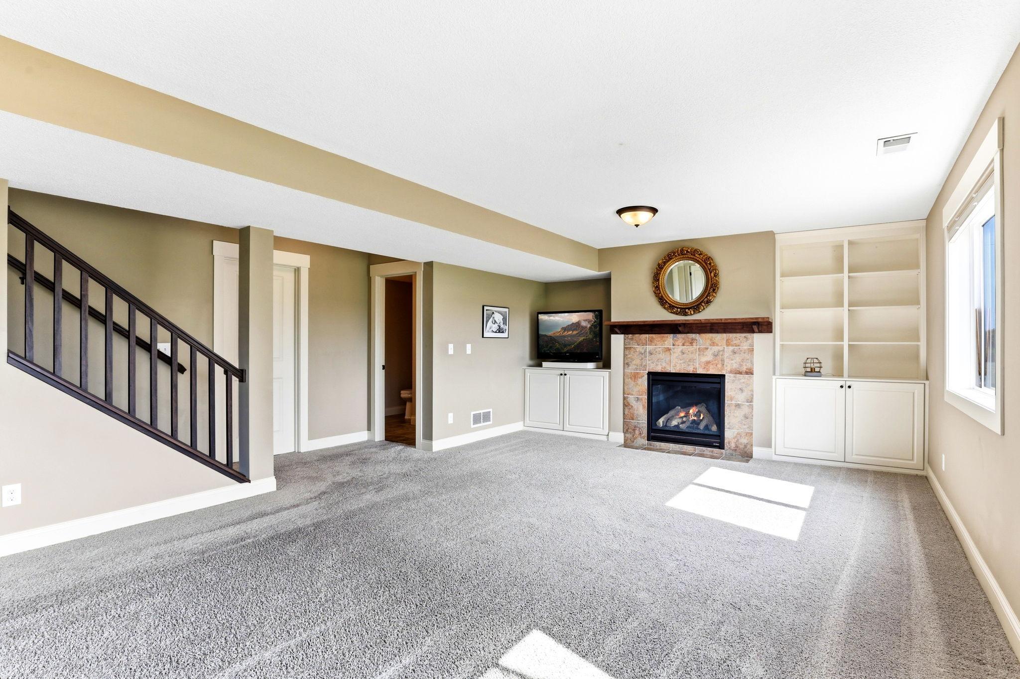 Finished walkout basement featuring a cozy tile-surround fireplace with custom built-in cabinetry and shelving.