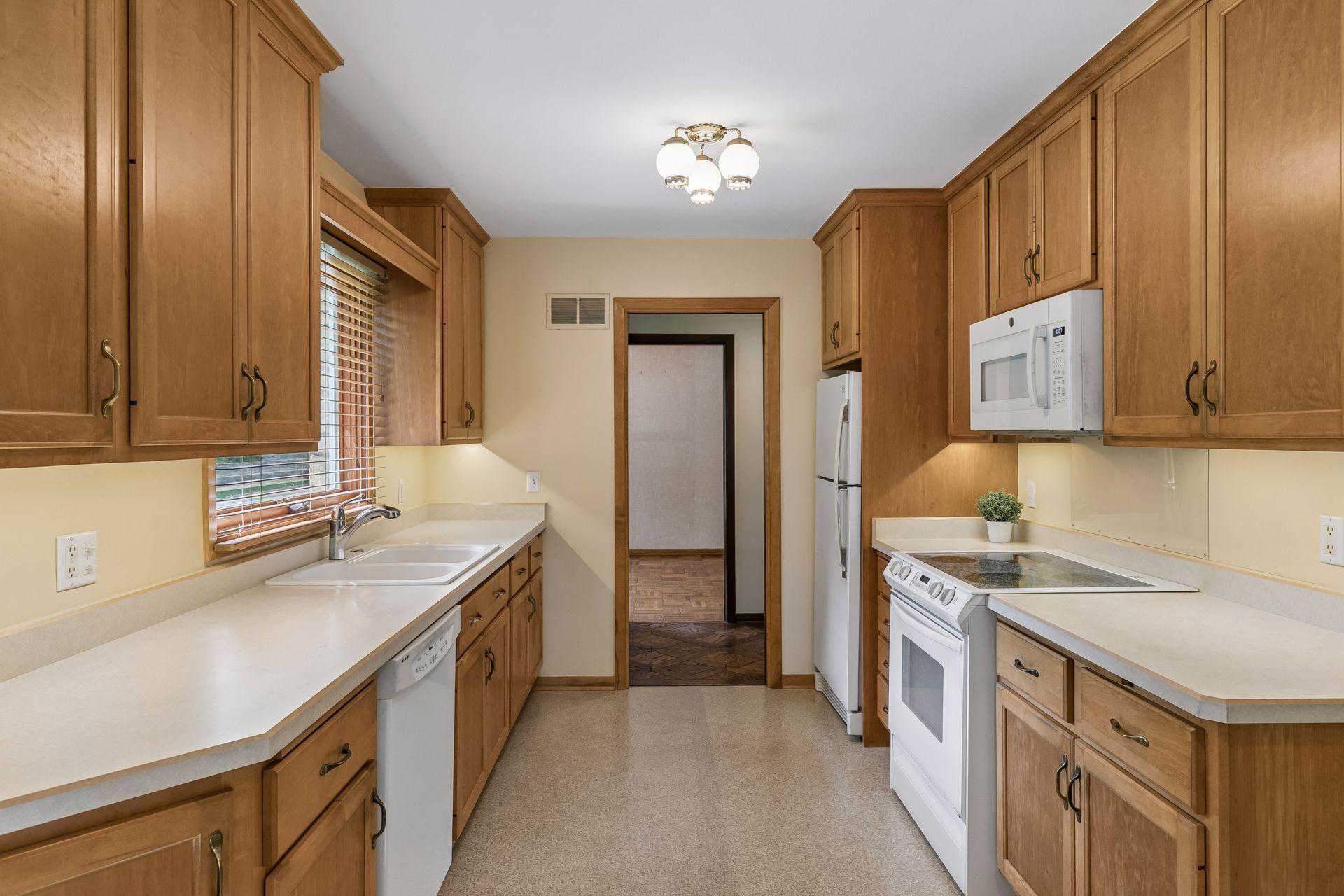 Classic galley kitchen with warm wood cabinetry, ample prep space, abundant storage, and natural light. Functional design with everything within easy reach.