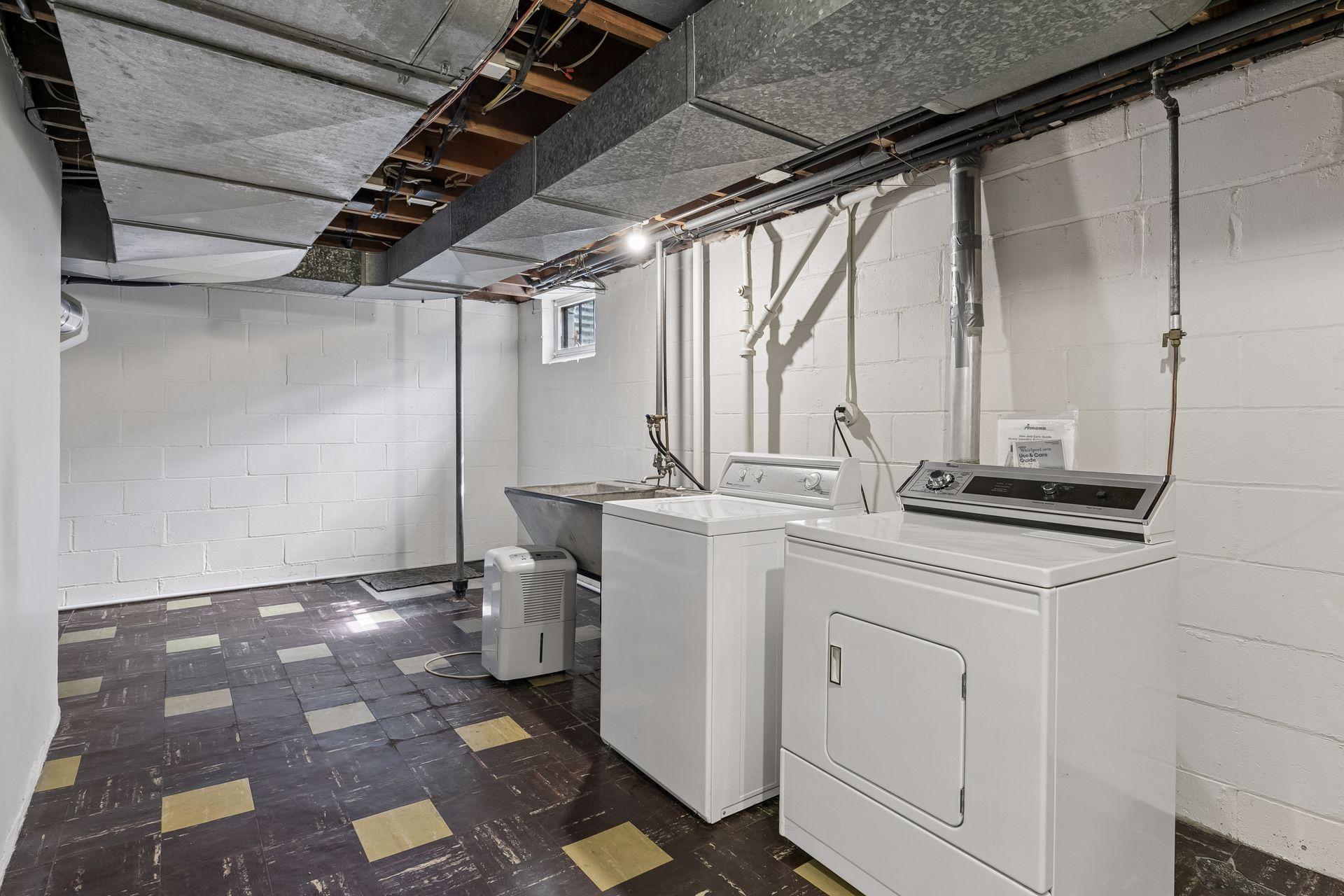 Half of the lower level remains unfinished, housing the laundry area with a classic concrete utility sink and flexible space for storage or future projects