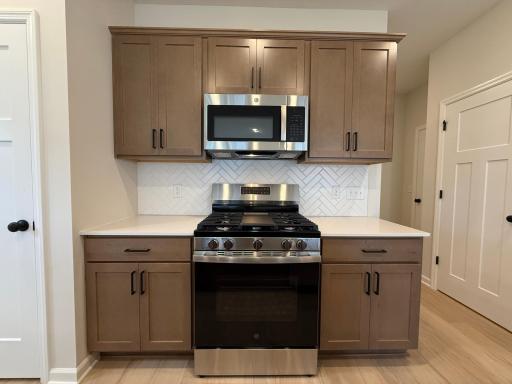 Gas range and overhead microwave make cooking a breeze with plenty of working space and a herringbone style tile backsplash