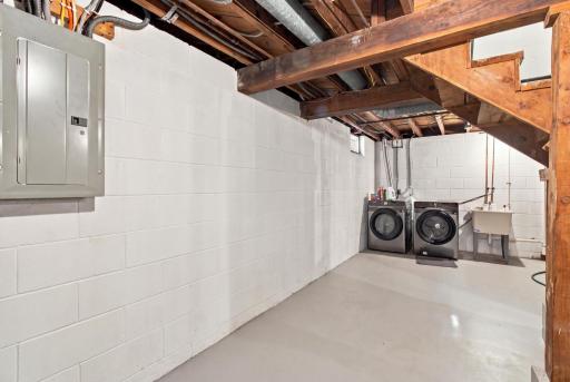 Lower level laundry. Electrical panel, washer and dryer, and a utility sink along the block wall.